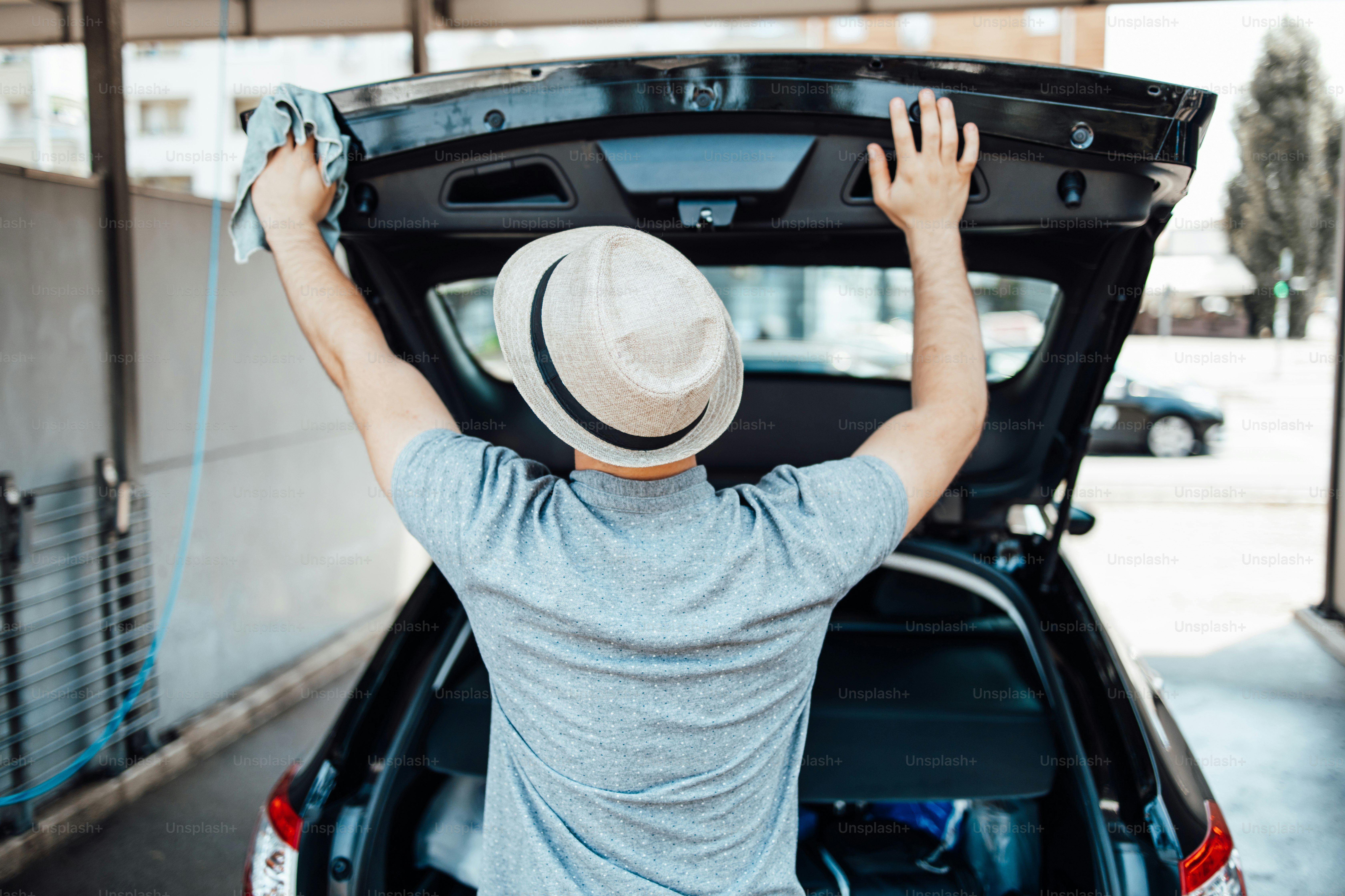 Junger gutaussehender Mann mit Hutputzauto mit Lappen, Autodetaillierung (oder Valeting) Konzept.