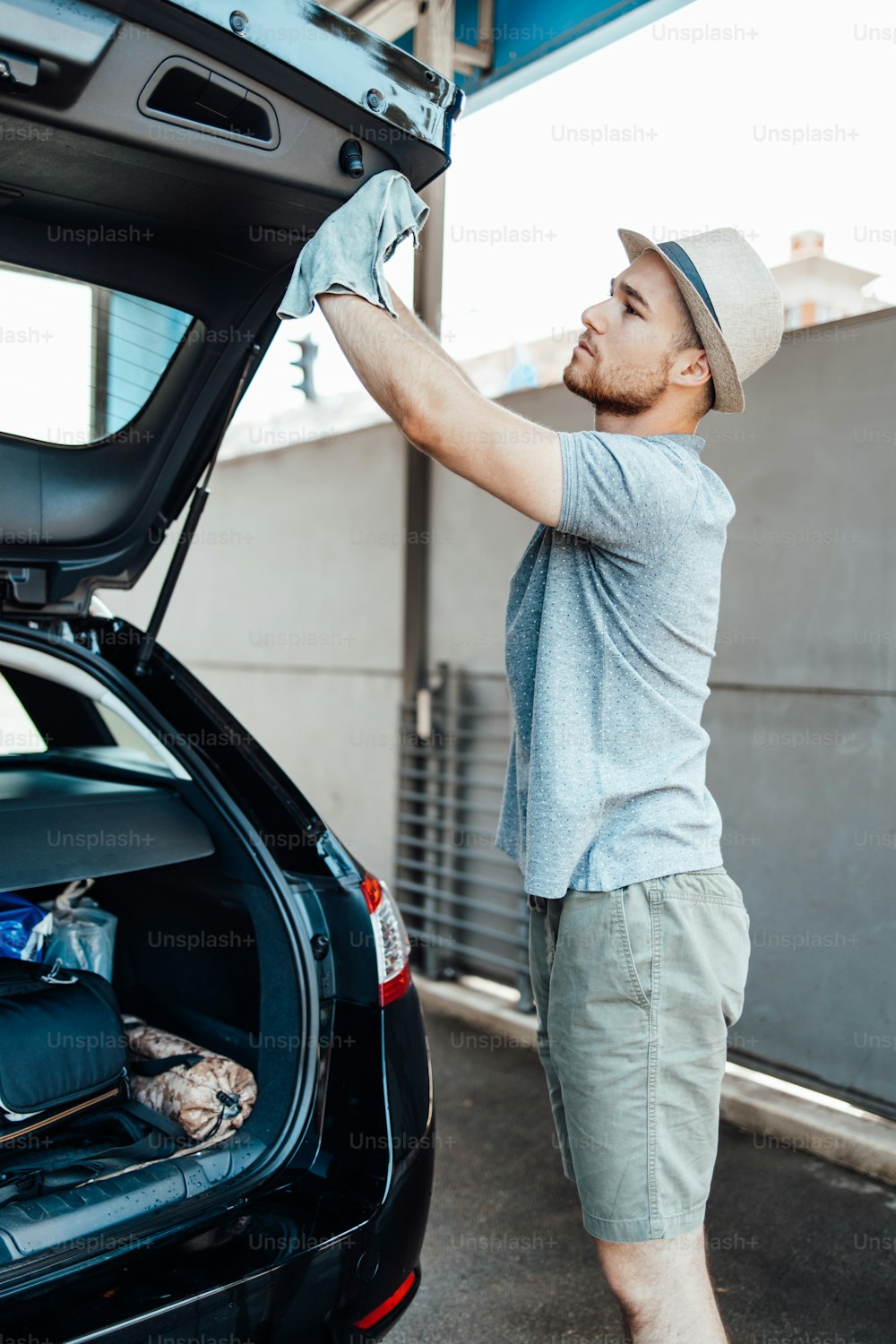 Joven guapo con sombrero limpiando el coche con el trapo, concepto de detalle del coche (o valeting).