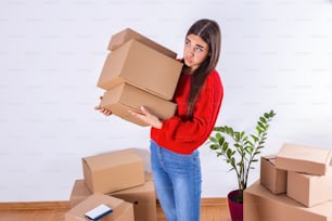 Young woman just moved in into new empty apartment unpacking and cleaning - relocation. Young girl carrying cardboard boxes at new home.Moving house.