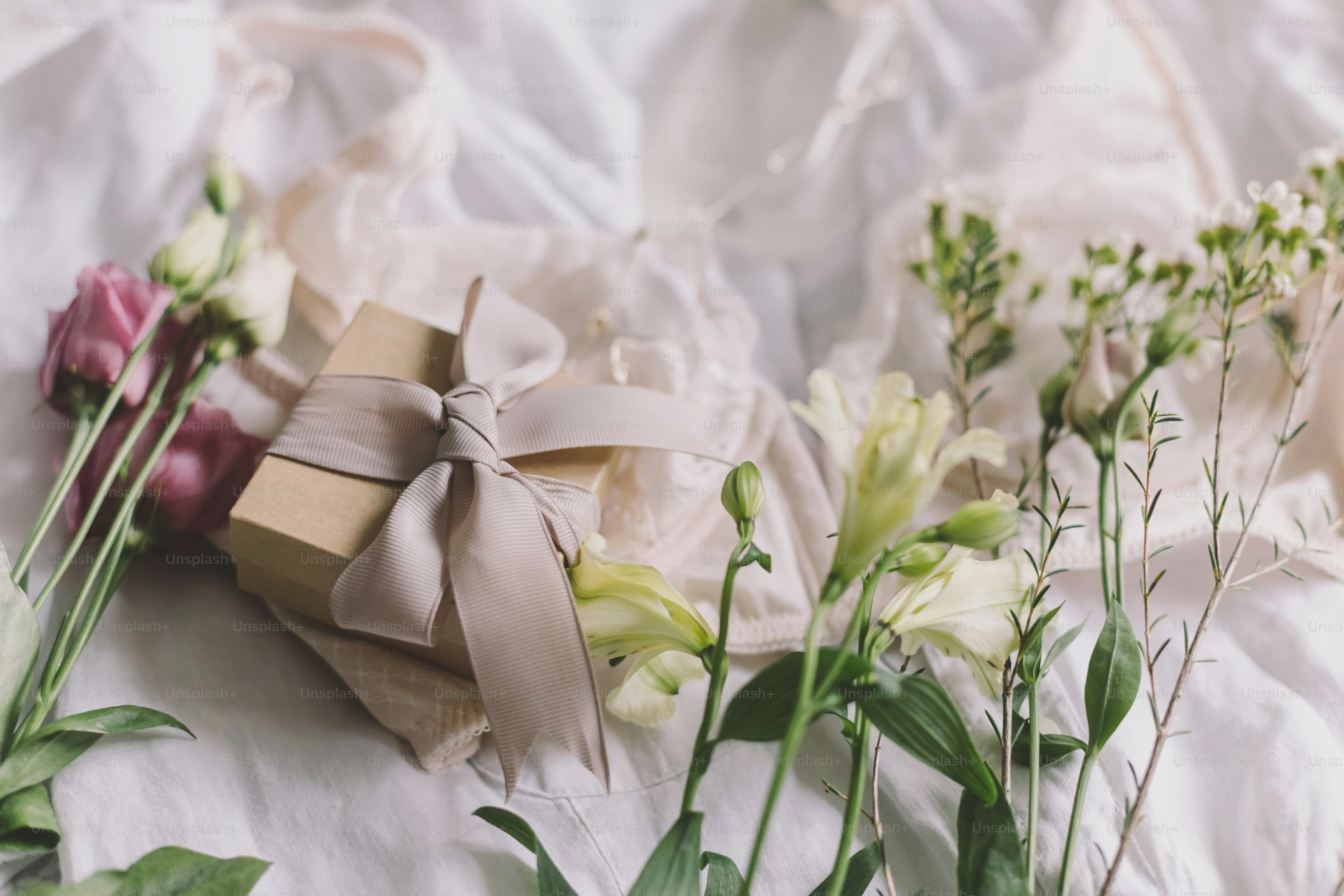 Stylish gift box, modern jewelry, lace lingerie and spring flowers on bed. Soft trendy feminine image, sensual mood at home concept. Happy Women's day. Woman essentials