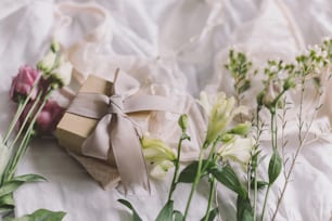 Stilvolle Geschenkbox, moderner Schmuck, Spitzendessous und Frühlingsblumen auf dem Bett. Weiches trendiges feminines Bild, sinnliche Stimmung zu Hause Konzept. Frohen Frauentag. Frauen Essentials