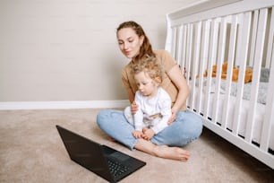 Young Caucasian mother with toddler baby boy watching cartoons on laptop at home. Family mom with kid using technology. Video chat, video call. Screen time for kids.