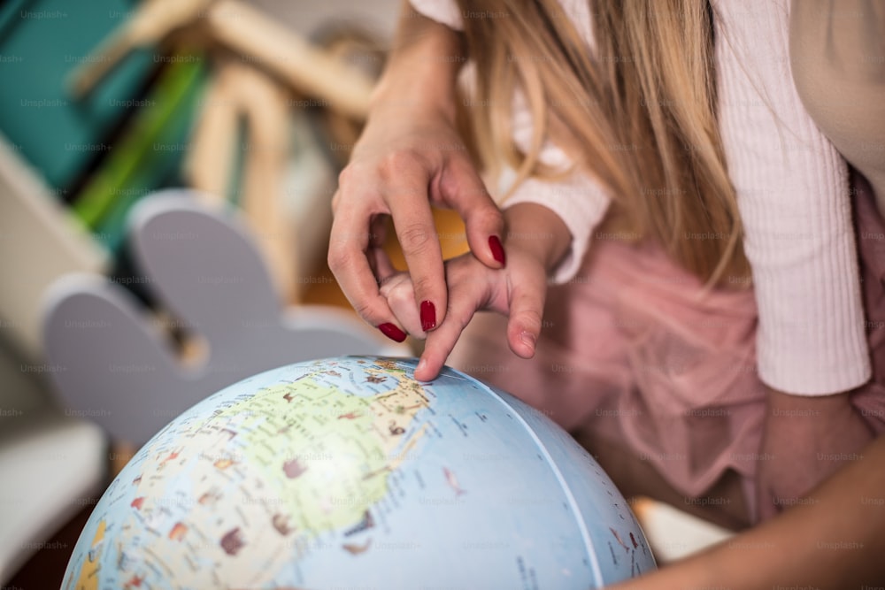 Mãe e filha aprendendo geografia em um globo mundial. O foco está nas mãos. De perto.