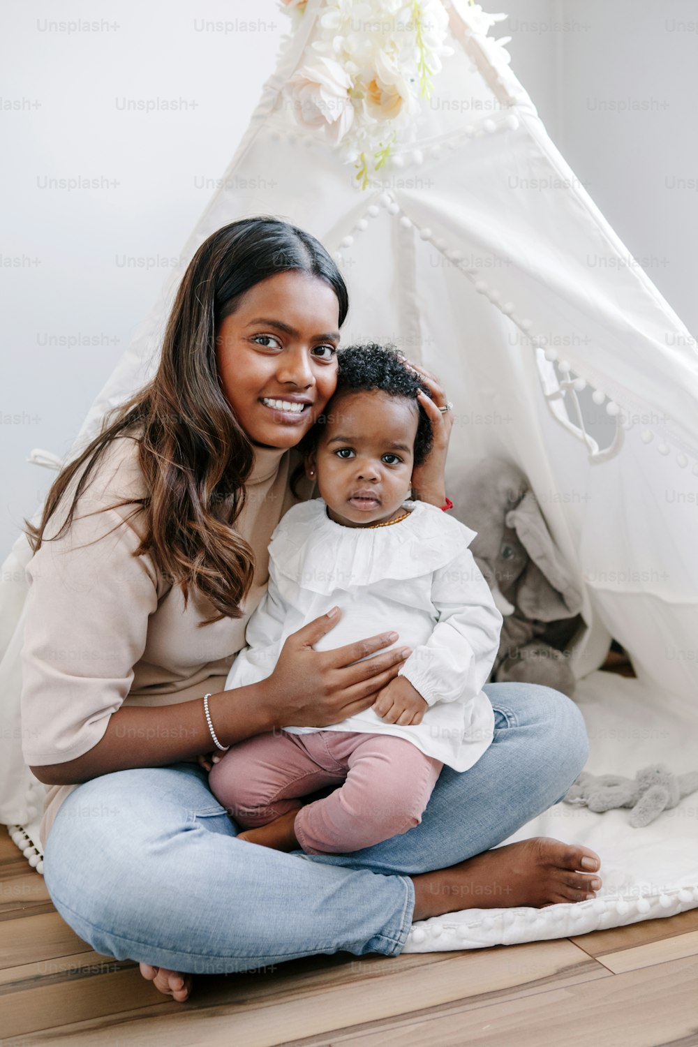 Happy smiling young Indian mother playing with black baby girl daughter. Family mixed race people mom and kid together hugging at home. Authentic candid lifestyle with infant kid child.