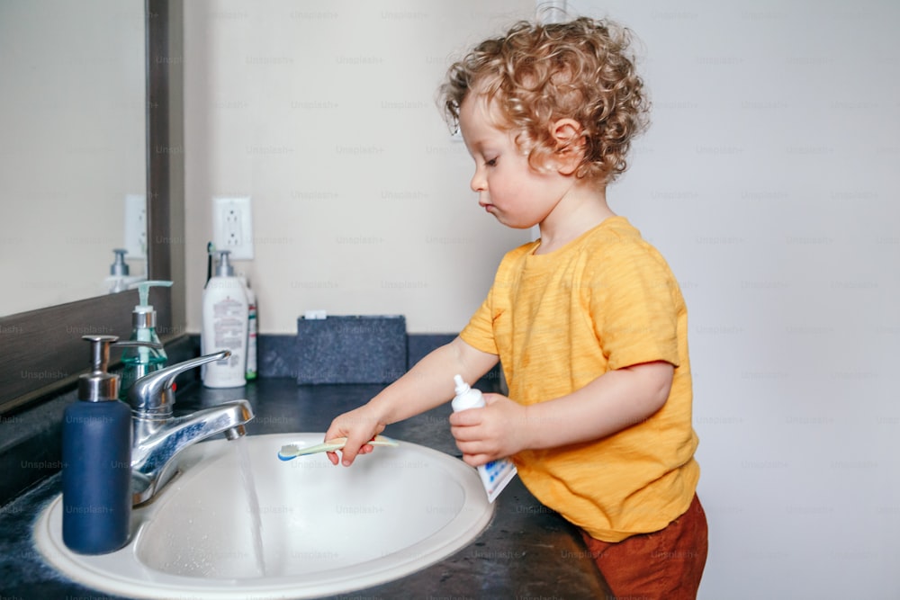 Little Caucasian boy toddler brushing teeth in bathroom at home. Health hygiene and morning routine for children. Cute funny child kid washing in toilet room.