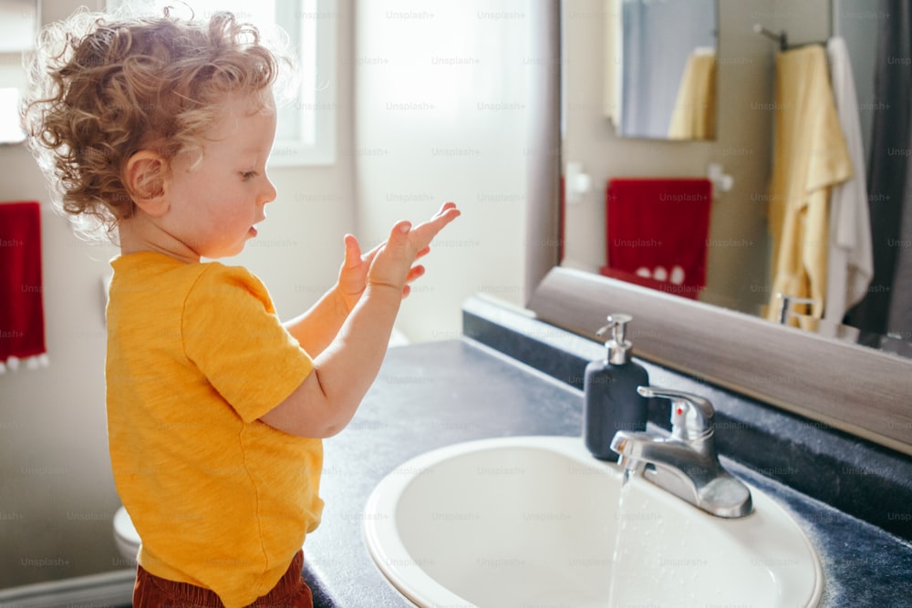 Piccolo bambino caucasico che si lava le mani nel bagno di casa. Igiene sanitaria e routine mattutina per i bambini. Bambino simpatico e divertente che gioca con l'acqua. Bambino che impara ad esplorare il suo corpo.