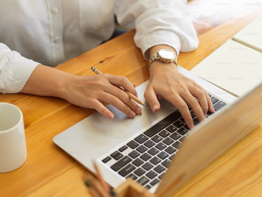 Cropped shot of female hands typing on laptop keyboard and working with stationery on wooden table