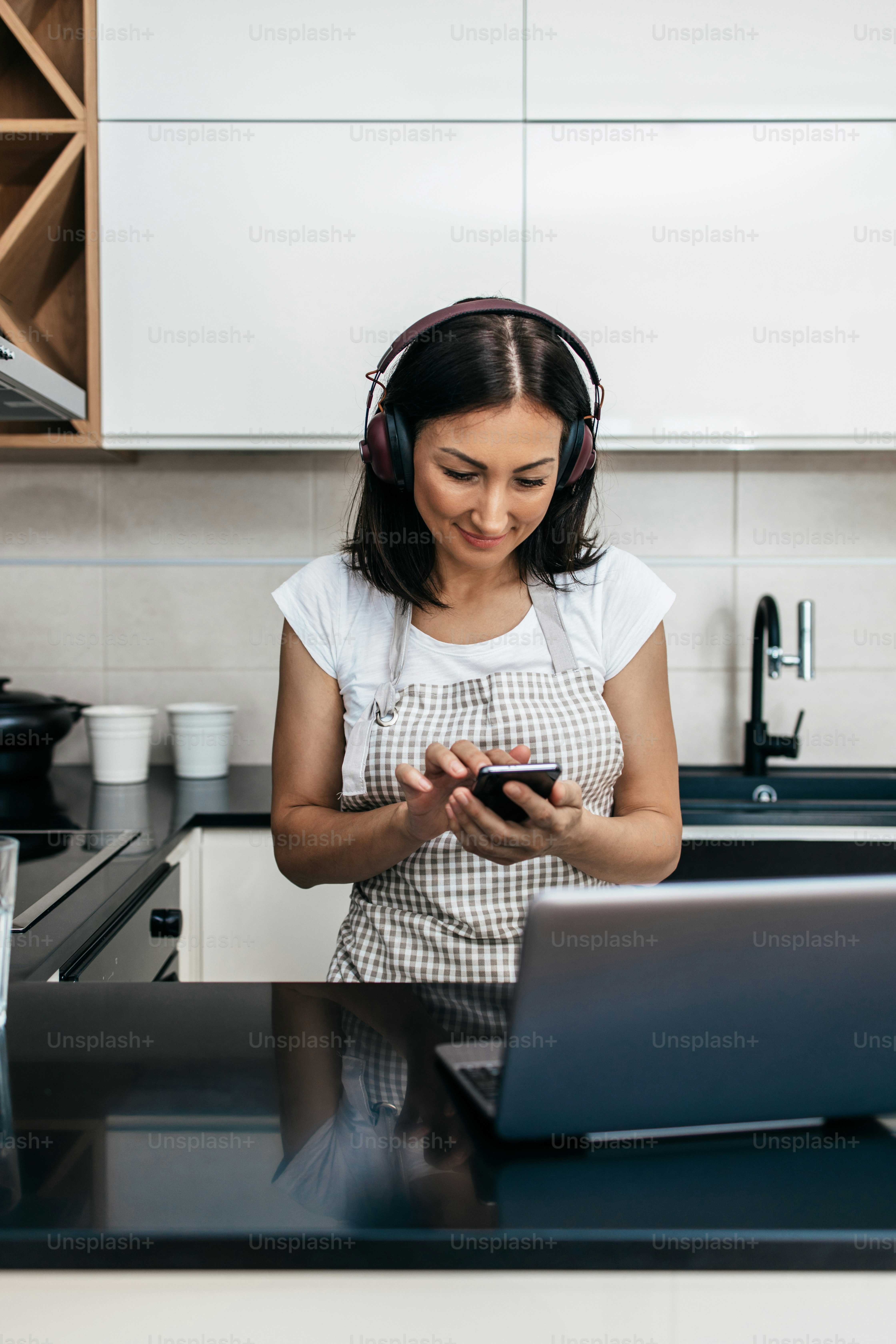Beautiful middle age woman sitting alone in her apartment. She gets bored but tries to have a good time and stay positive. She uses laptop computer and tablet to chat and listen to music.