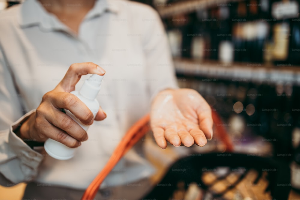 Jeune femme élégante dans une épicerie utilisant un spray désinfectant pour se désinfecter les mains. Plan rapproché. Thème de la pandémie de coronavirus.