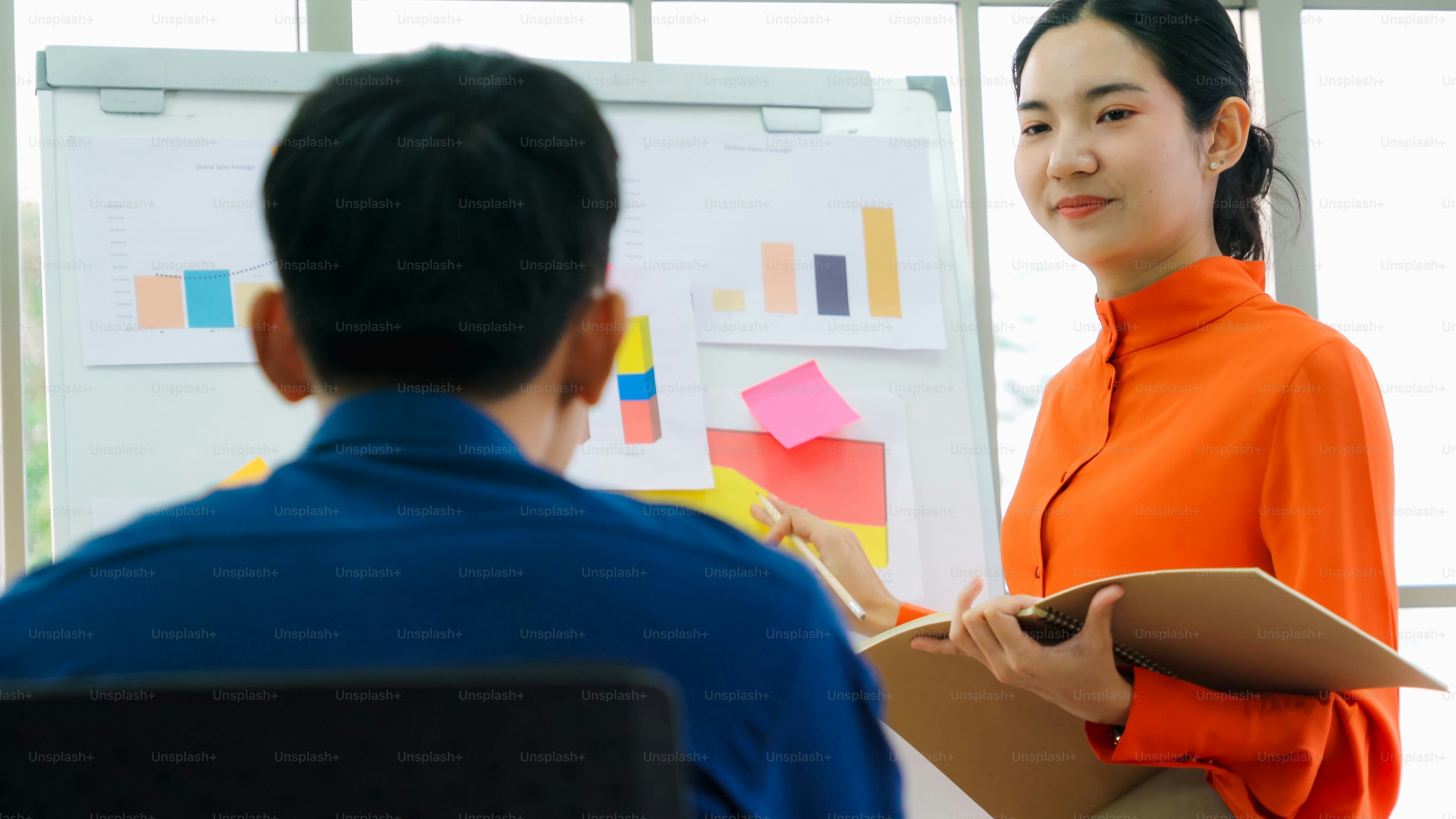 Young woman explains business data on white board in casual office room . The confident Asian businesswoman reports information progress of a business project to partner to determine market strategy .