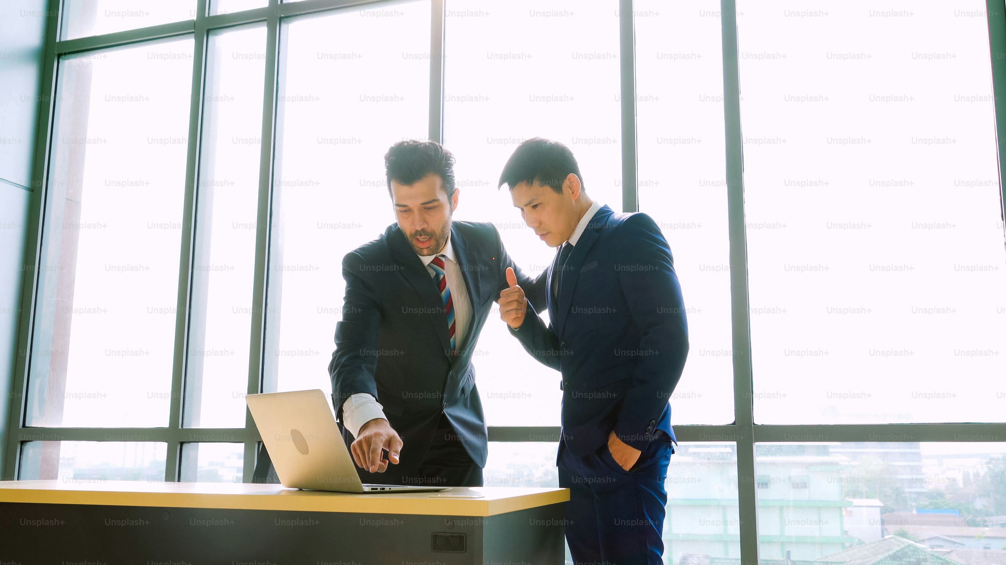 Deux hommes d’affaires discutent de stratégie de projet dans une salle de réunion de bureau. L’homme d’affaires discute de la planification du projet avec un collègue sur un lieu de travail moderne tout en ayant une conversation et des conseils sur le rapport de données financières.