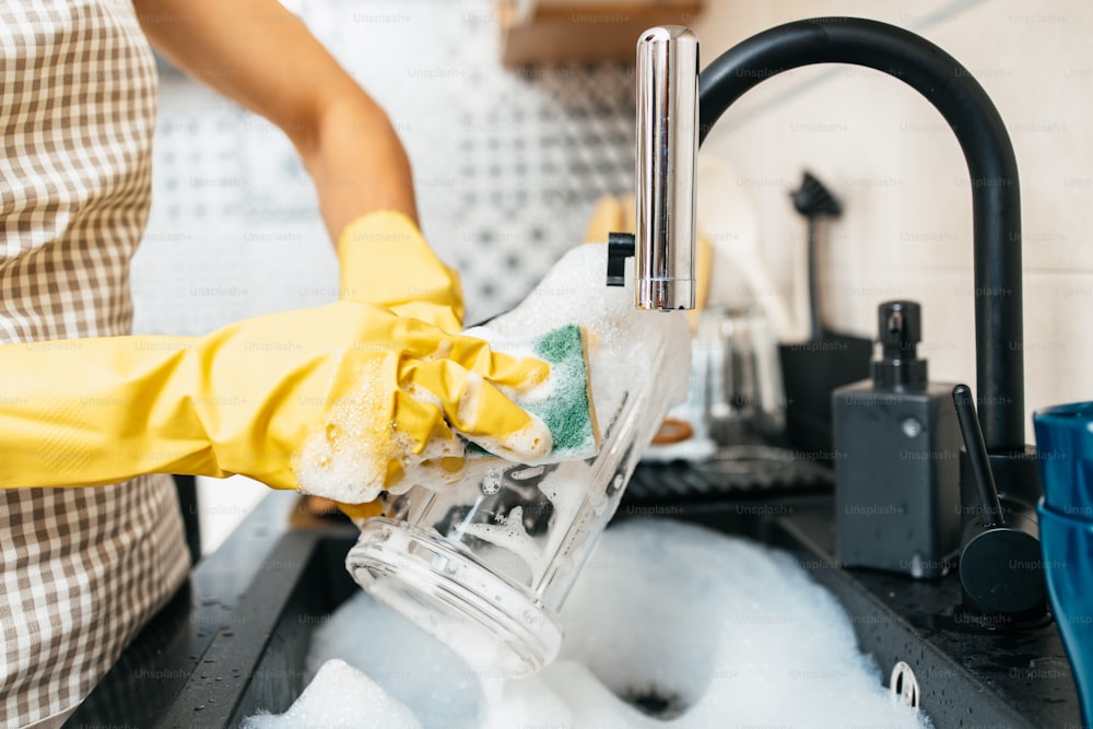 Young adult woman with yellow protective gloves washing her dishes on kitchen sink. Household and home hygiene routine.