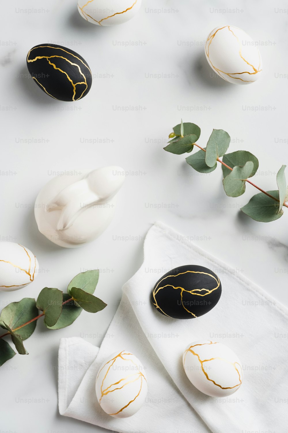 Elegant Easter flat lay composition. Stylish Easter eggs decorated with gold, rabbit bunny, eucalyptus leaves on marble table. Top view. Minimal style.