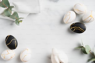 Composition de luxe de Pâques à plat avec des œufs noirs et dorés, des feuilles d’eucalyptus, un lapin lapin, une serviette sur une table en marbre. Joyeuses Pâques concept. Vue de dessus.