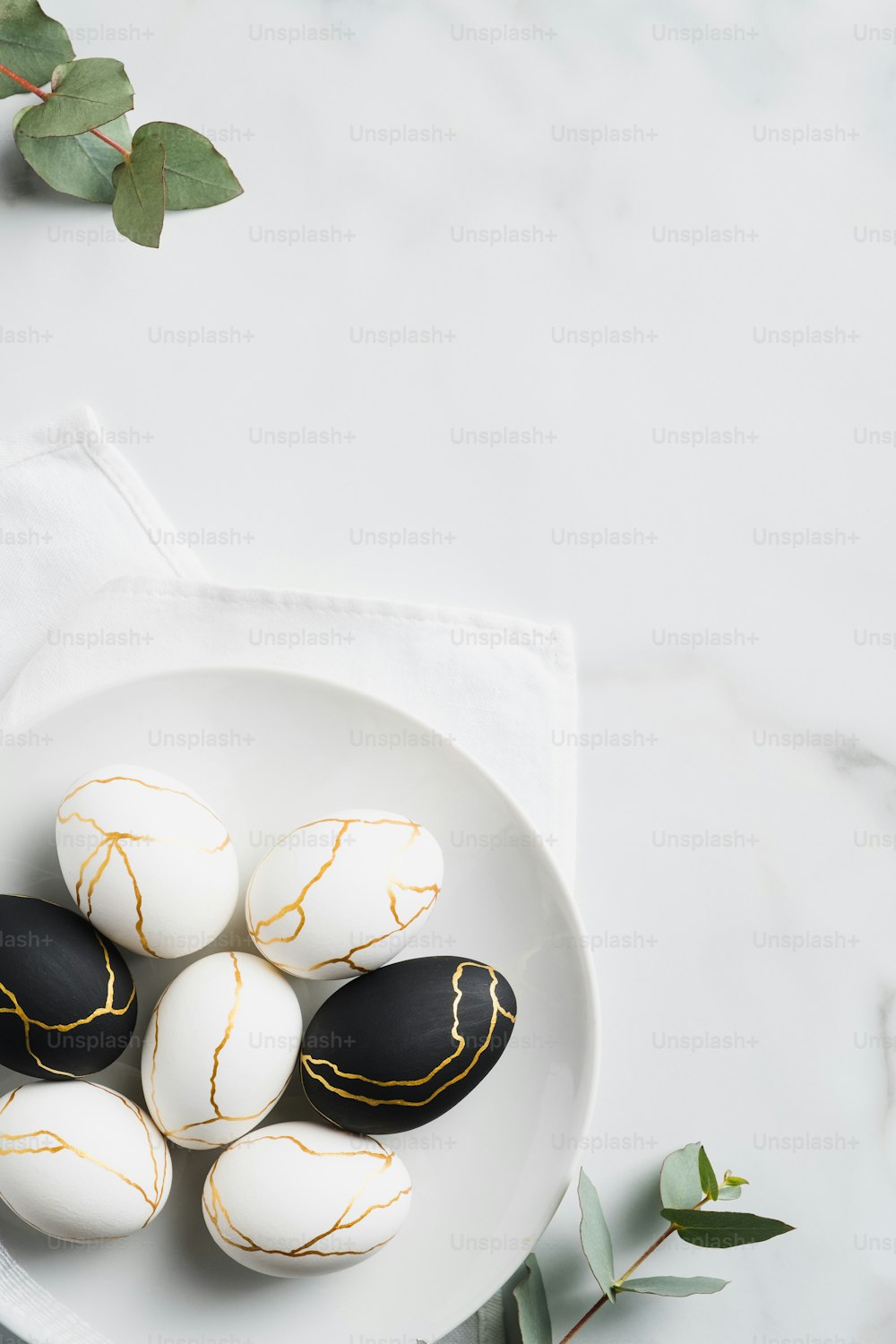 Luxury Easter eggs decorated with gold in plate and eucalyptus leaves on marble table. Flat lay, top view. Minimal style.