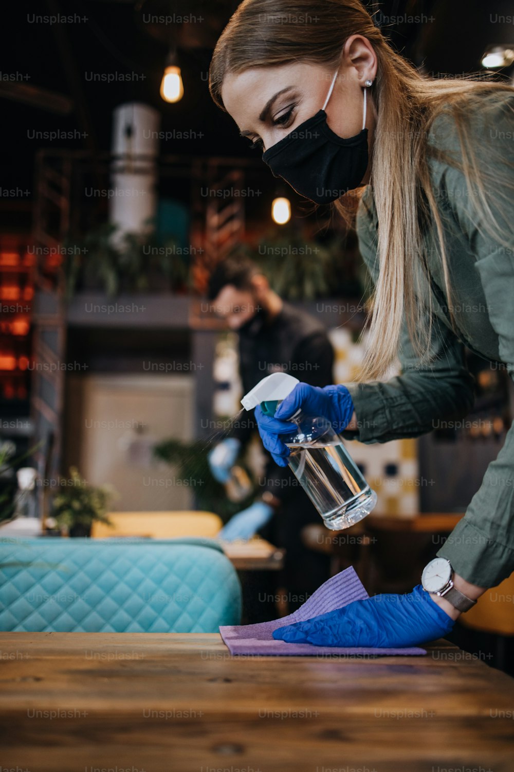 Jóvenes camareros de restaurantes limpiando y desinfectando mesas y superficies contra la enfermedad pandémica del Coronavirus. Llevan mascarillas protectoras y guantes.