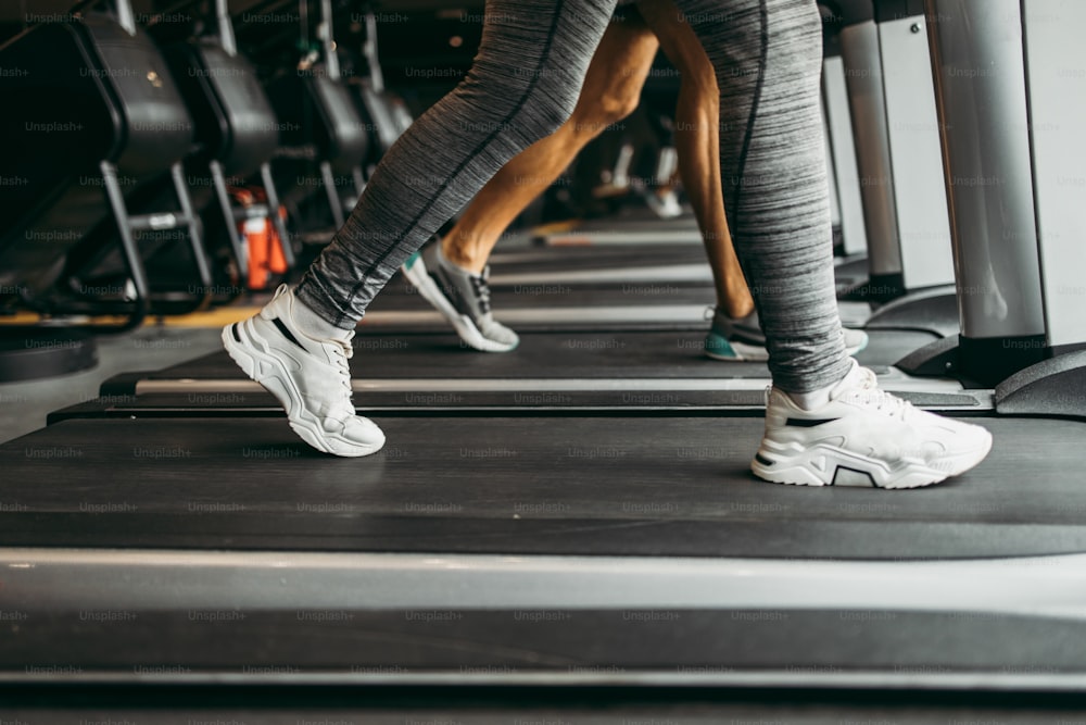 Young fit woman and man running on treadmill in modern fitness gym. They keeping distance and wearing protective face masks. Coronavirus world pandemic and sport theme.