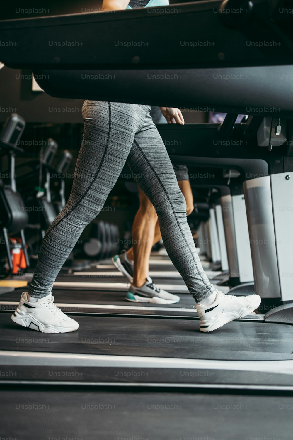 Young fit woman and man running on treadmill in modern fitness gym. They keeping distance and wearing protective face masks. Coronavirus world pandemic and sport theme.