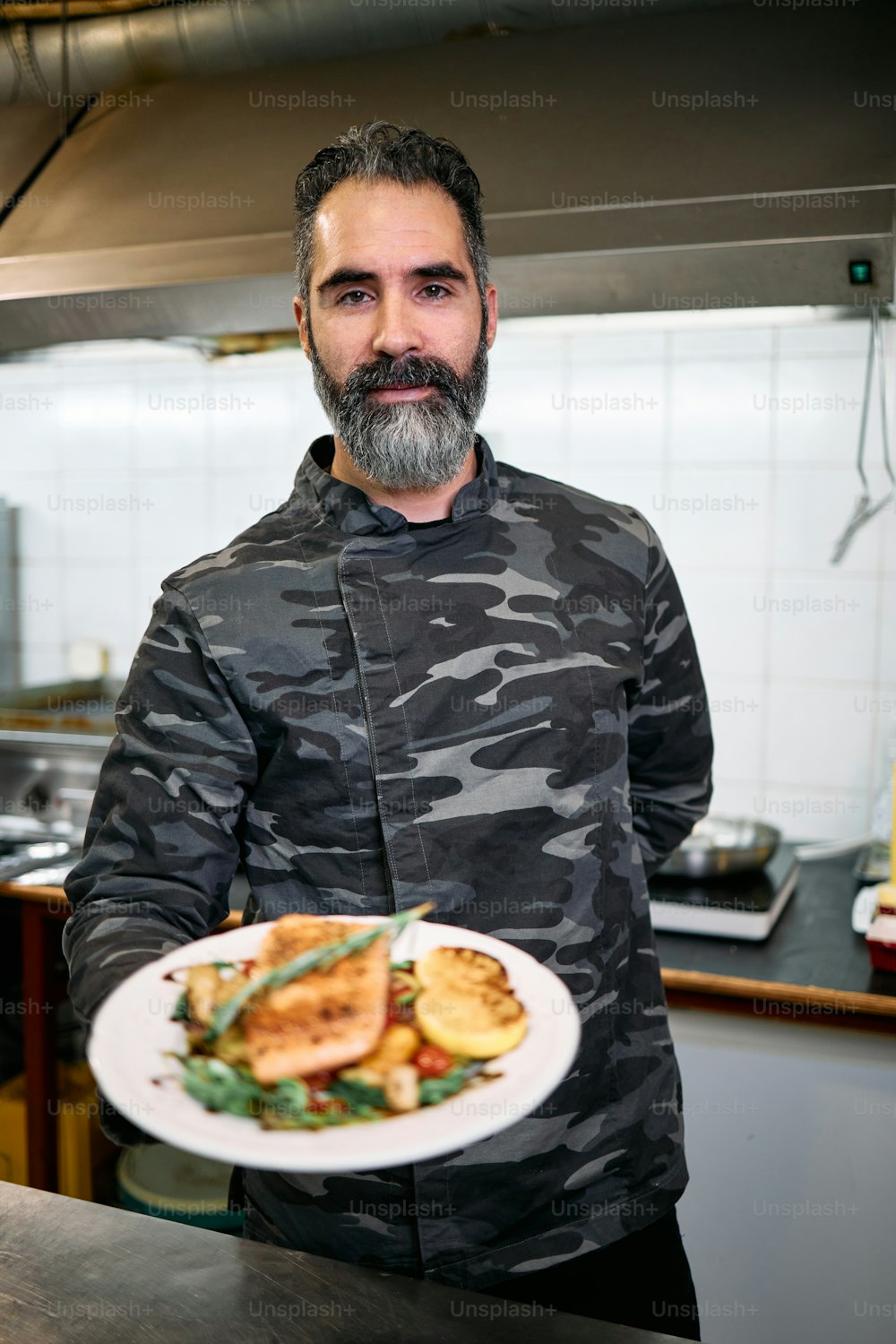 Professioneller Militärbasiskoch oder Koch hält köstliche leckere Mahlzeiten mit frischem Lachsfisch und Salat. Er posiert und schaut in die Kamera.