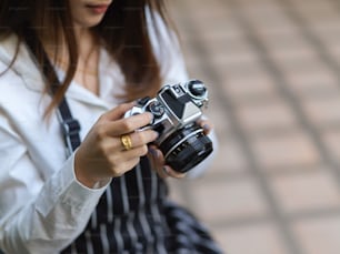 Foto recortada de una fotógrafa con delantal comprobando la imagen en la cámara digital mientras toma una foto en el café