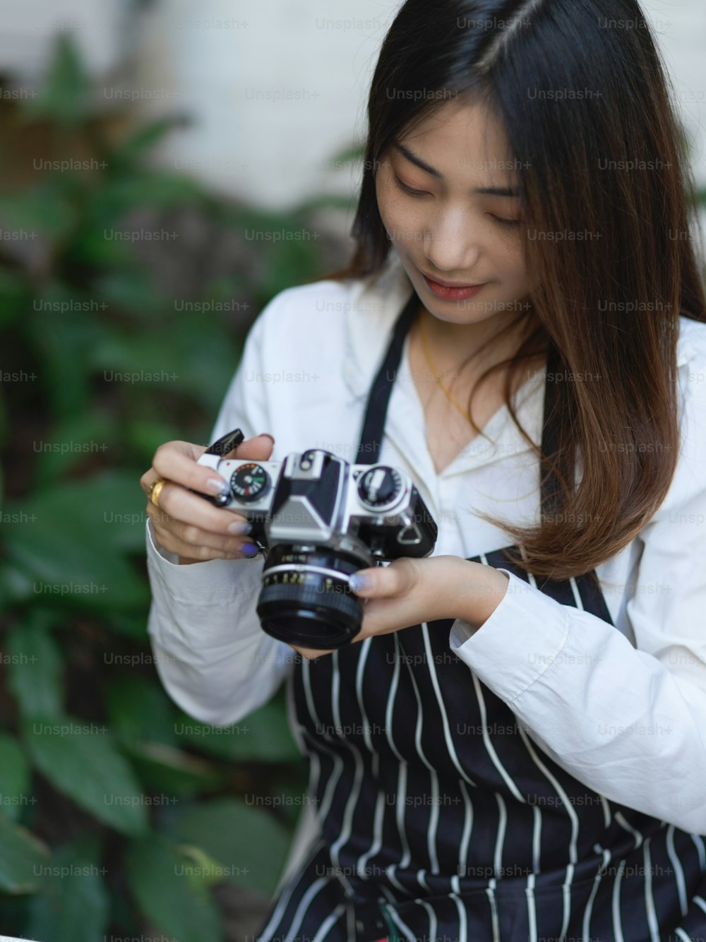 Retrato de una fotógrafa femenina con delantal comprobando la imagen en la cámara digital mientras toma una foto en el café