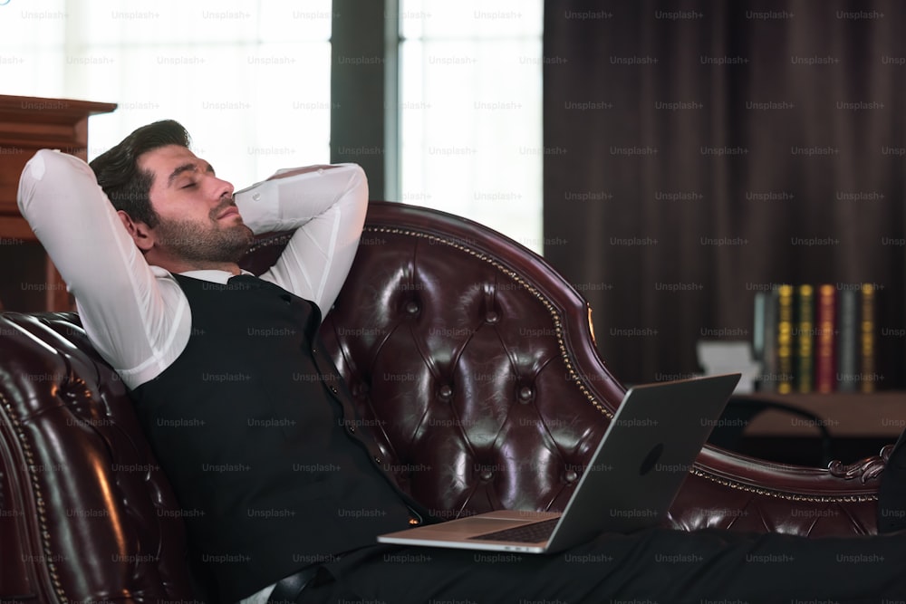 Businessman lying on sofa and Holding Laptop Computer.