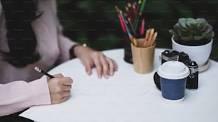 Cropped shot of young female holding pencils drawing picture on empty paper and sitting at backyard.