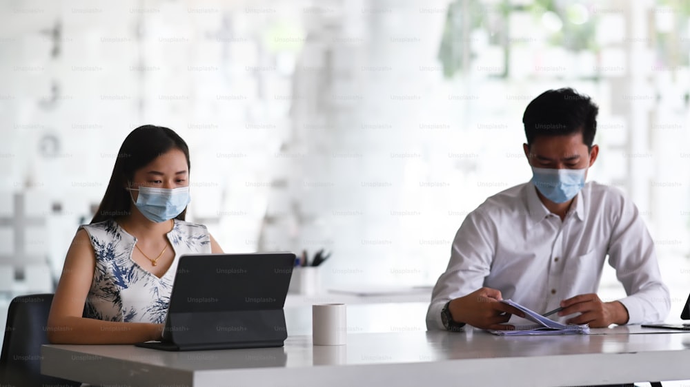 Two businesspeople wearing protective mask working and discussing project together in office.