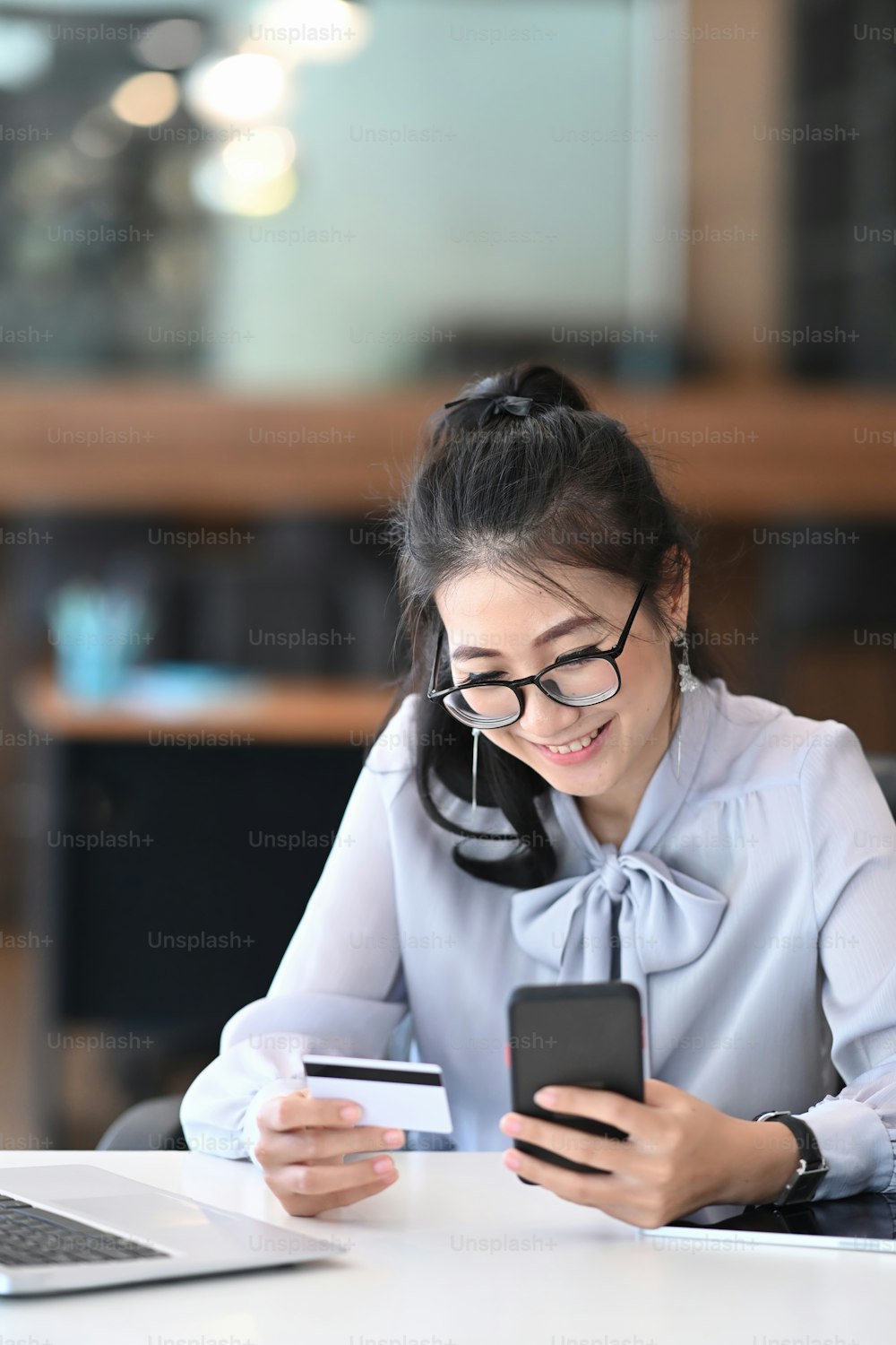 Mujer de negocios sonriente sosteniendo la tarjeta de crédito y usando el teléfono inteligente para compras en línea o factura de pago.