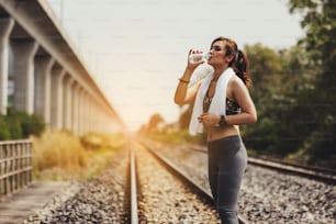 Sportswoman drinking water at old railway track for workout and exercise