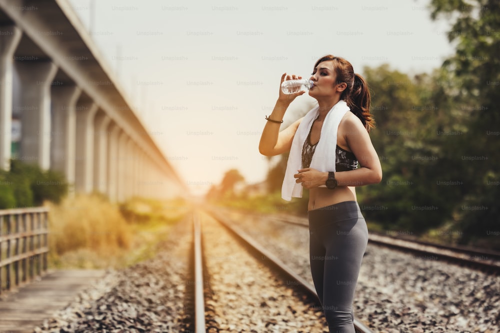 Sportswoman drinking water at old railway track for workout and exercise