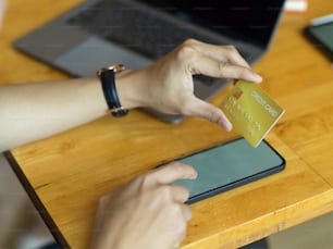 Colpo ritagliato di mano maschile che tocca lo smartphone e tiene la carta di credito durante il pagamento online