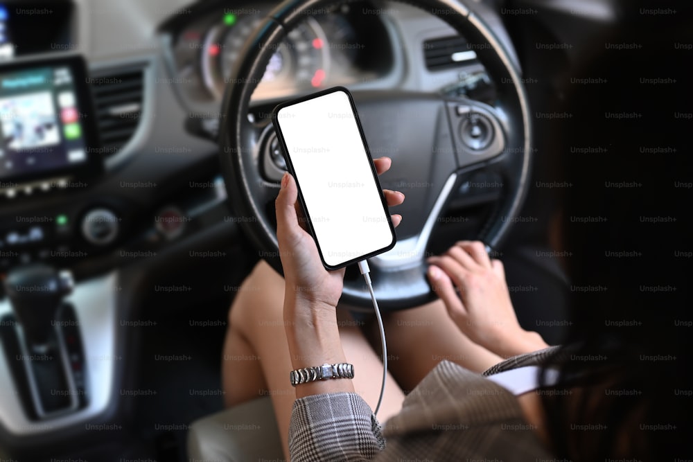 Ausschnittaufnahme einer jungen Frau, die ein Smartphone benutzt, während sie im Auto sitzt.