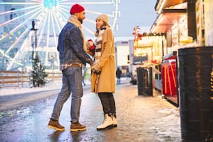 幸せな愛する若い男性と女性は、プレゼントを持って市内中心部を歩き、冬には観覧車に行きます