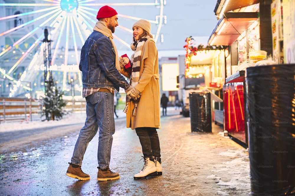Un jeune homme et une jeune femme heureux et aimants se promènent dans le centre-ville avec des cadeaux et vont à la grande roue en hiver