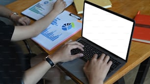 Foto recortada de empresarios trabajando en una computadora portátil y analizando documentos en la sala de reuniones.