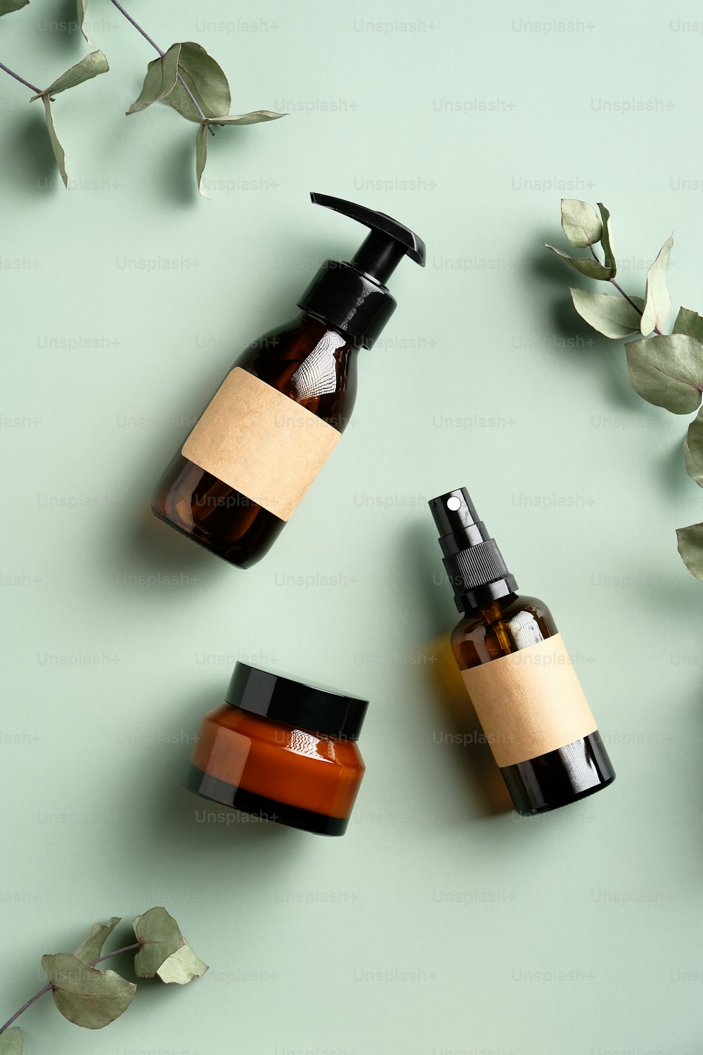 SPA cosmetics products branding mockup. Flat lay amber glass shampoo dispenser, spray bottle, jar of moisturizer cream and eucalyptus leaves on green background. Natural organic skincare products set