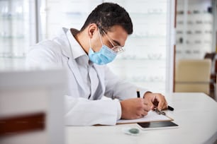 Vue latérale d’un opticien masculin concentré écrivant avec un stylo sur une feuille de papier
