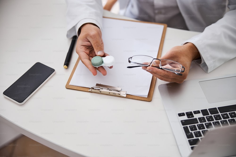 Cropped photo of an optometrist holding a plastic lens case and a pair of spectacles