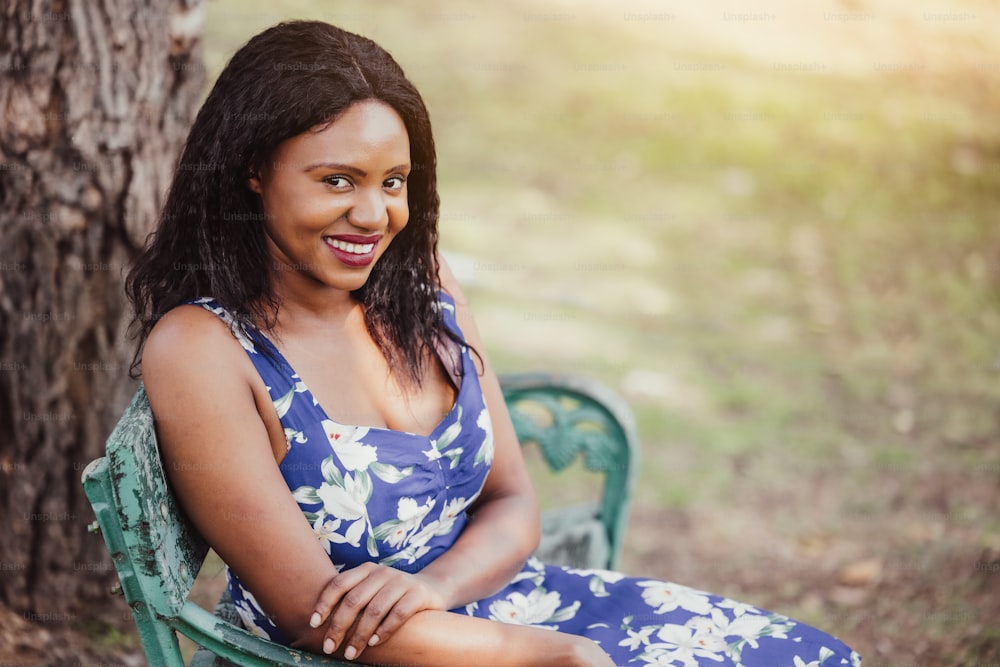 Black woman seated alone on a bench at the park, Pretty dark-skinned female sitting in the park relaxing. People, emotion and lifestyle concept.