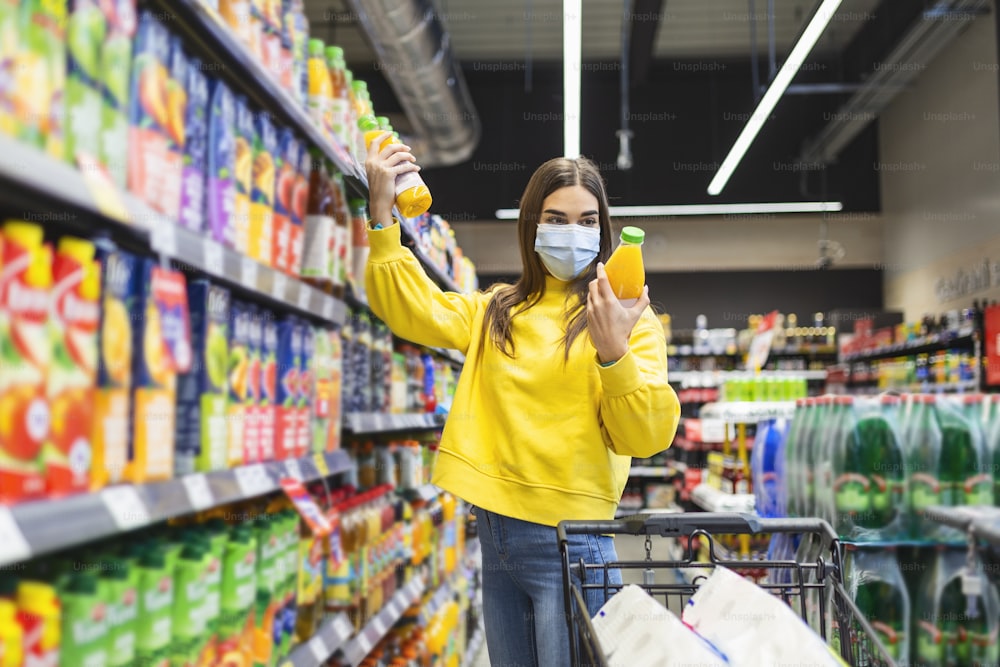 Junger Mensch mit Schutzmaske beim Einkauf von Lebensmitteln im Supermarkt. Vorbereitung auf eine pandemische Quarantäne aufgrund des Coronavirus-Covid-19-Ausbruchs. Auswahl von nicht verderblichen Lebensmittel-Essentials Stockfoto