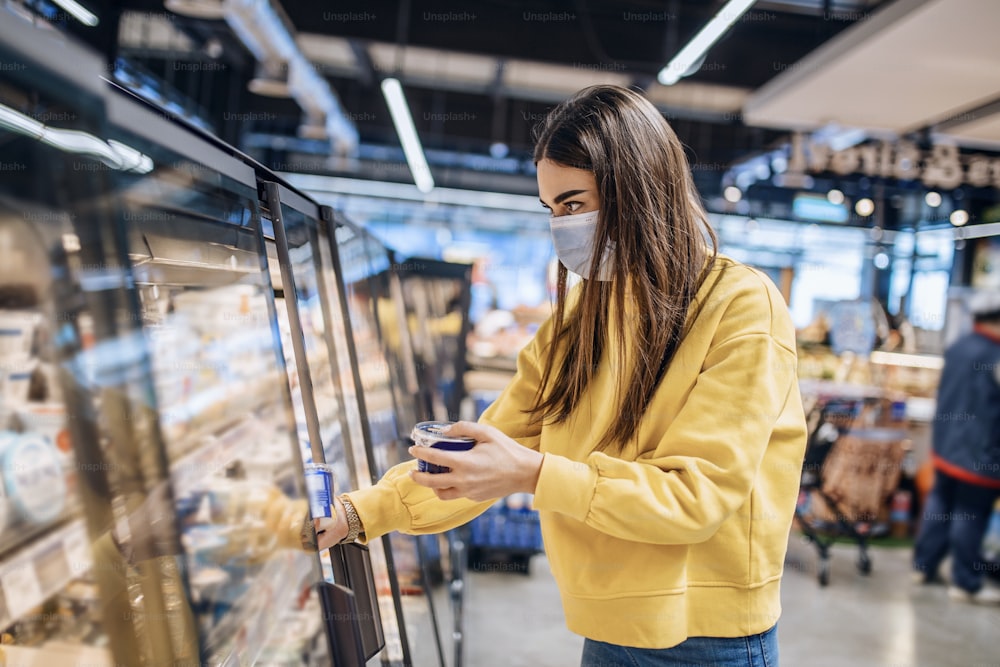 Woman wearing face mask buying in supermarket.Panic shopping during Coronavirus covid-19 pandemic.Budget buying at a supply store.Buying freezer smart purchased household pantry groceries