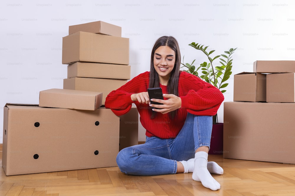 Young woman moving to a new apartment. Typing a message while sitting down