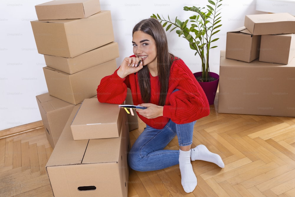 A young beautiful women makes her notes and plans in her new flat,apartment. Young woman packing cardboard box. Moving house concept.