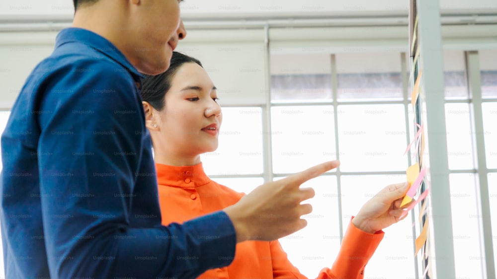 Os empresários trabalham no quadro de planejamento de projetos no escritório e conversam com colegas de trabalho para analisar o desenvolvimento do projeto. Eles usam notas adesivas afixadas na parede de vidro para torná-lo organizado.