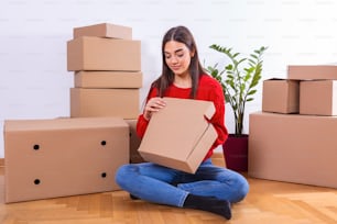 Young woman packing boxes, moving to new apartment. Young woman moving new place and repair concept - happy young woman with many cardboard boxes sitting on floor