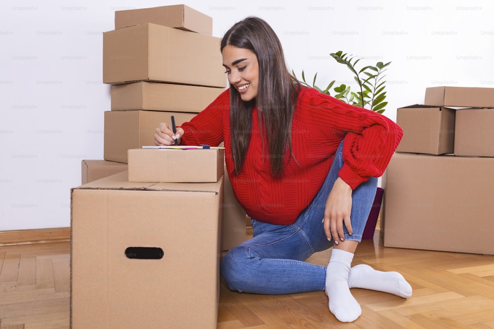 Mujer joven que mueve nuevo lugar y concepto de reparación - mujer joven feliz con muchas cajas de cartón sentadas en el piso de casa