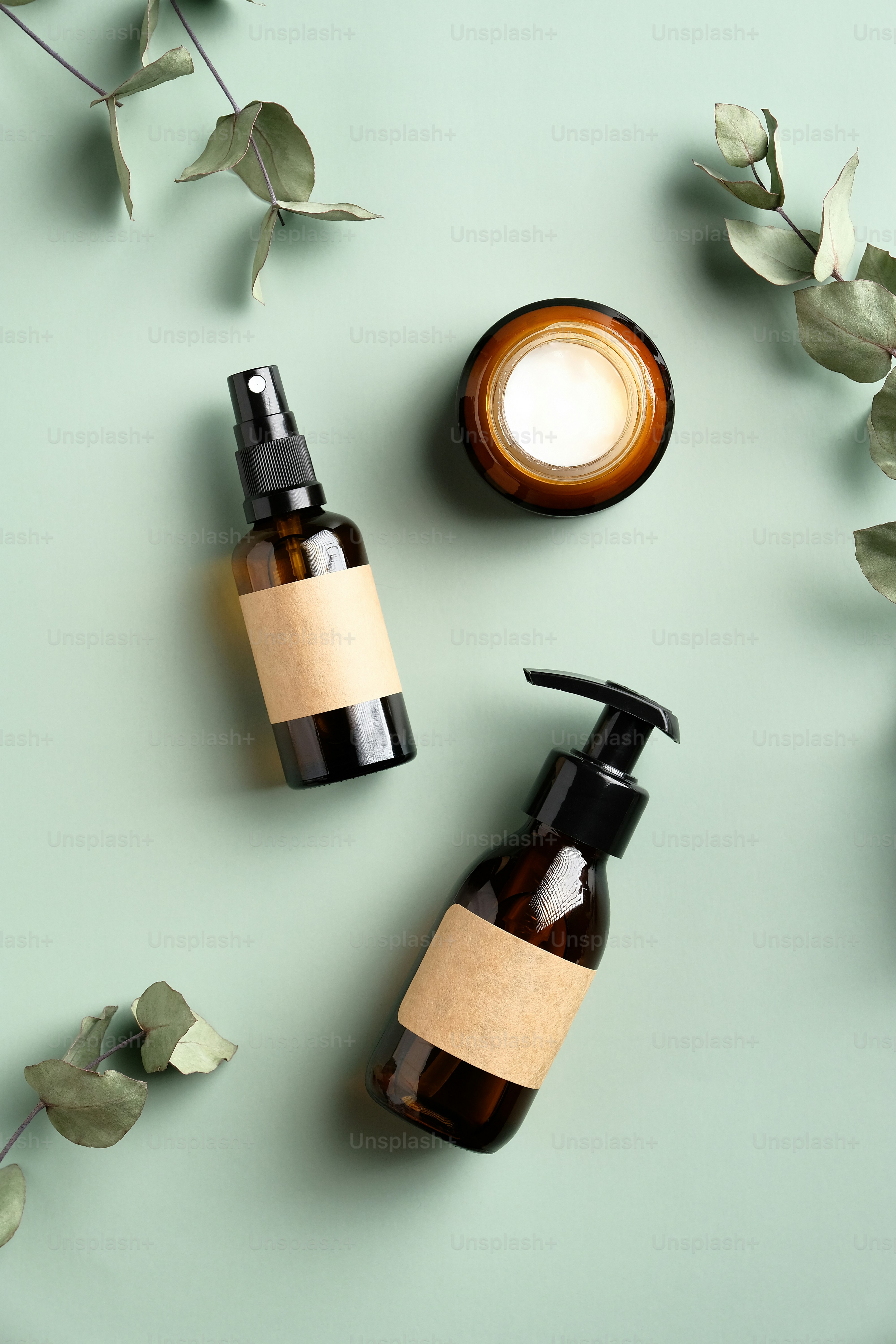 Natural organic SPA cosmetic products set with eucalyptus leaves. Top view amber glass dispenser with homemade shampoo, spray bottle, moisturizer cream jar on green background. Flat lay minimal style.