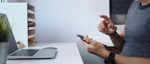 Abgeschnittene Aufnahme eines Mannes, der auf einem Smartphone eine SMS mit der Hand schreibt, während er am Arbeitsplatz sitzt.