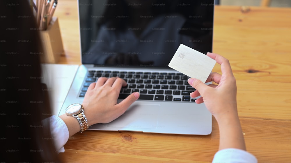 Vue arrière d’une jeune femme utilisant un ordinateur portable et tenant une carte de crédit effectuant un paiement en ligne ou des achats en ligne.